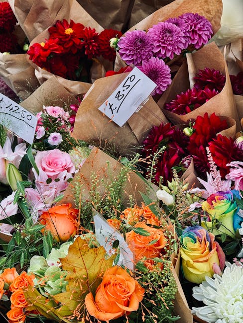 A vibrant assortment of freshly prepared floral bouquets displayed together outdoors, featuring a variety of flowers including pink roses, orange roses, deep red dahlias, purple chrysanthemums, and wh